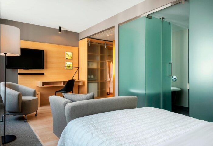 Le Méridien Vienna gay-friendly hotel room. Modern design with desk, TV, closet, and frosted glass bathroom. Upscale gay travel lodging.