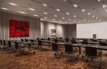 Le Meridien Vienna gay-friendly hotel meeting room. Tables and chairs face a screen. Art adorns the walls. Parquet floor.