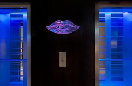 Le Méridien Vienna's stylish elevator lobby. A purple lips art piece adorns the wall between two elevators with blue lighting. Gay-friendly hotel.
