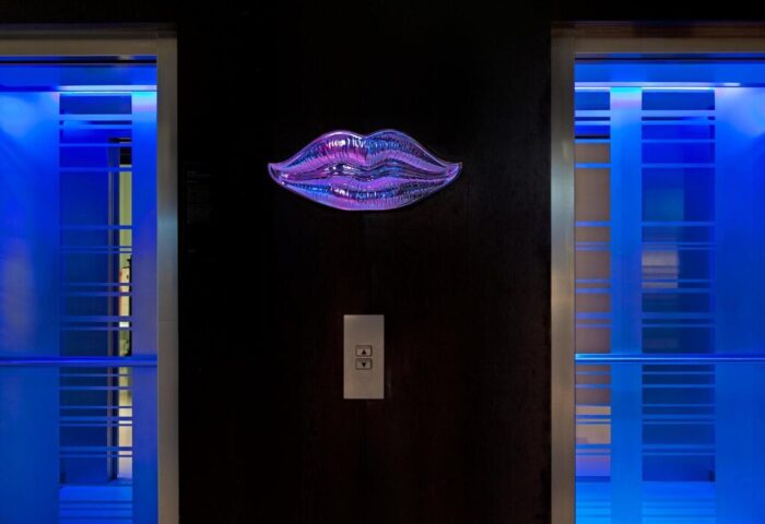 Le Méridien Vienna's stylish elevator lobby. A purple lips art piece adorns the wall between two elevators with blue lighting. Gay-friendly hotel.