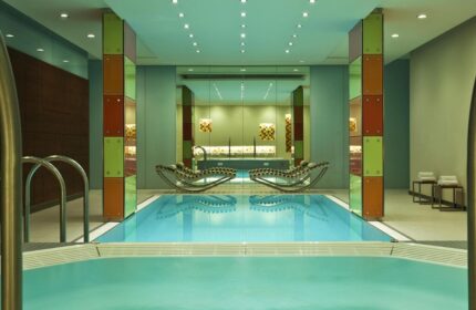 Le Méridien Vienna gay-friendly hotel indoor pool. Modern design with colorful accents. Loungers reflect in the water. Upscale gay travel.