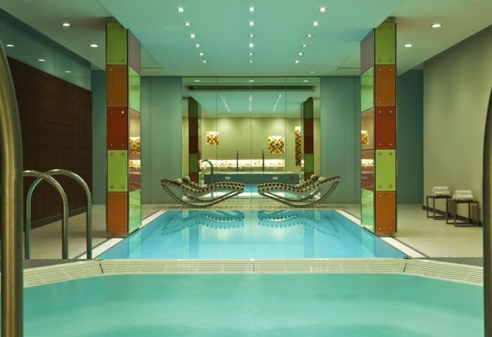 Le Méridien Vienna gay-friendly hotel indoor pool. Modern design with colorful accents. Loungers reflect in the water. Upscale gay travel.
