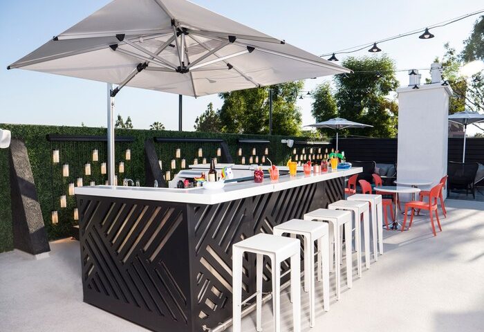 Le Parc at Melrose gay-friendly hotel bar. Outdoor bar with stools, cocktails, umbrella, and lights. Great spot for gay travelers.