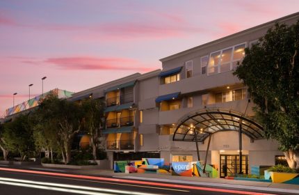 Le Parc at Melrose, a gay-friendly hotel. Exterior view of the hotel entrance at dusk, showcasing its modern architecture and colorful accents.