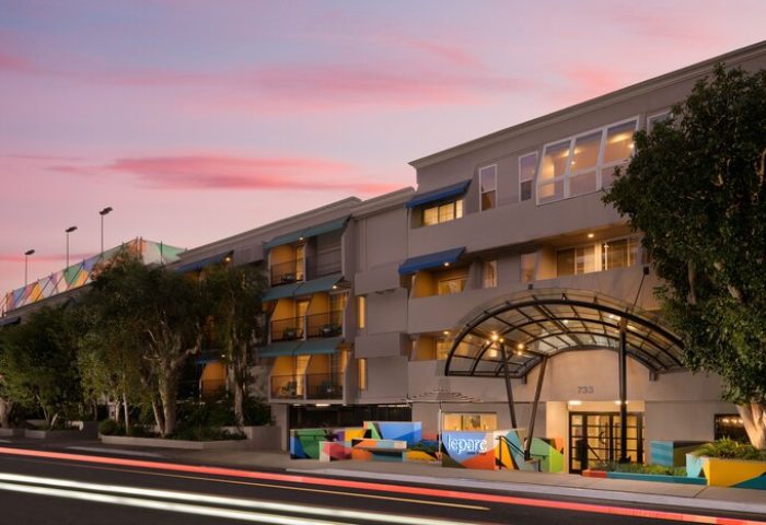 Le Parc at Melrose, a gay-friendly hotel. Exterior view of the hotel entrance at dusk, showcasing its modern architecture and colorful accents.