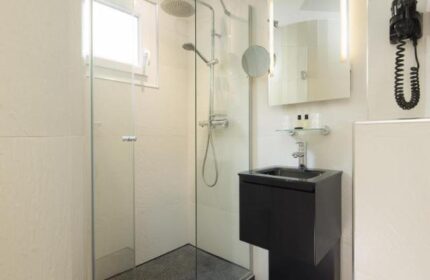 Bathroom at Le Relais du Marais Hotel, a gay-friendly hotel. Features a glass shower, black sink, mirror, and hair dryer. Modern design.