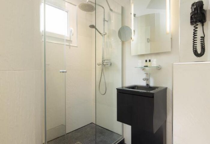 Bathroom at Le Relais du Marais Hotel, a gay-friendly hotel. Features a glass shower, black sink, mirror, and hair dryer. Modern design.