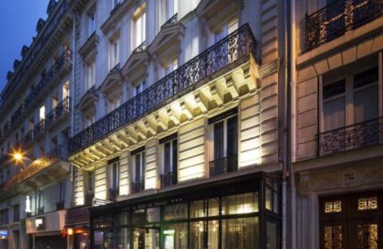 Le Relais du Marais Hotel, a gay-friendly hotel in Paris. Building exterior at dusk with wrought iron balconies and glass-enclosed entrance.