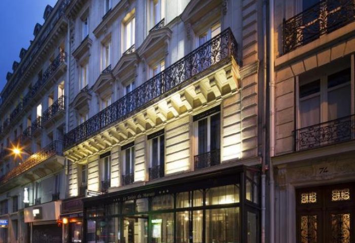 Le Relais du Marais Hotel, a gay-friendly hotel in Paris. Building exterior at dusk with wrought iron balconies and glass-enclosed entrance.