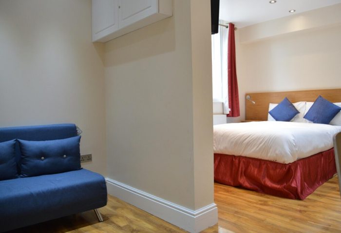 Le Ville Hotel gay-friendly room. View of the bed with blue pillows and red skirt, and a blue sofa in the living area. Hotel room interior.