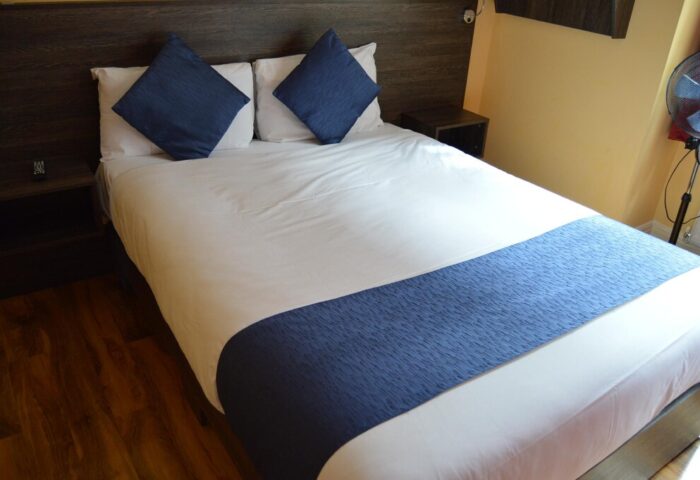 Le Ville Hotel room. Gay-friendly hotel bedroom with a bed with white sheets, blue pillows and a blue runner. Nightstands on either side.