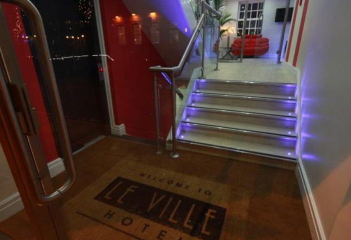 Entrance of Le Ville Hotel, a gay-friendly hotel. Steps with purple lighting lead to a stylish interior. Doormat with the hotel's name.