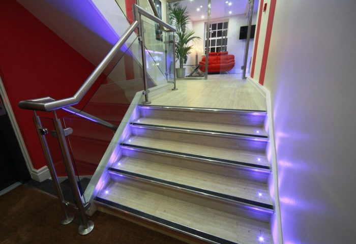 Stairway at Le Ville Hotel, a gay-friendly hotel. Modern design with glass railings and purple LED lighting. Red sofa visible in the background.