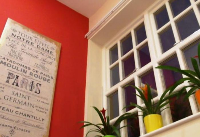 Le Ville Hotel's gay-friendly room decor: Paris themed art on red wall, window with plants. A stylish touch for gay men travelers.
