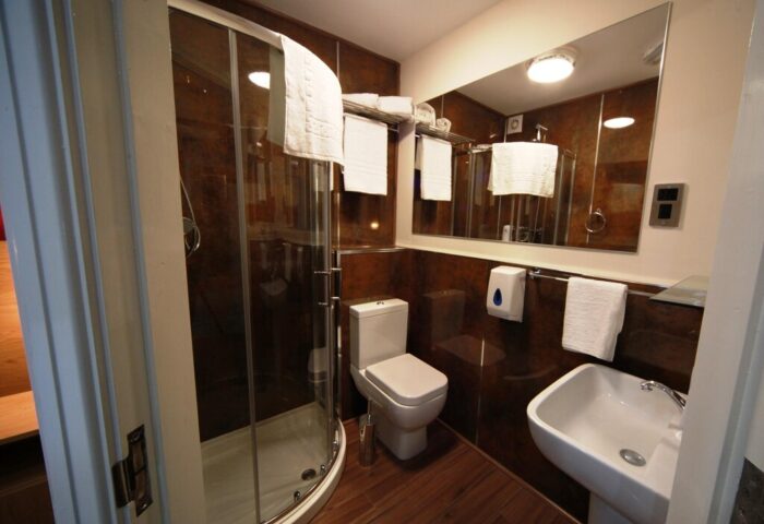 Le Ville Hotel bathroom. Shower, toilet, sink, mirror and towels in a gay-friendly hotel. Modern design, brown tile, clean and well-lit.
