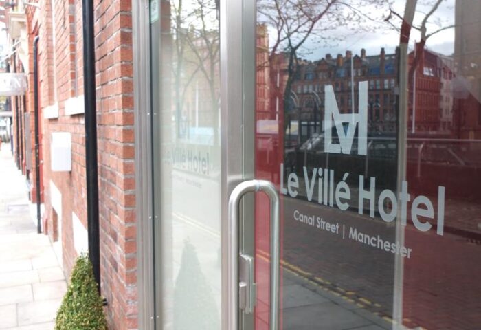 Entrance to Le Ville Hotel, a gay-friendly hotel in Manchester. Glass door with hotel name and Canal Street address. Brick building exterior.