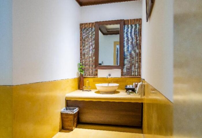 Le Vimarn Cottages & Spa bathroom. Modern sink, mirror, and woven blinds. Gay-friendly hotel bathroom with yellow accents.