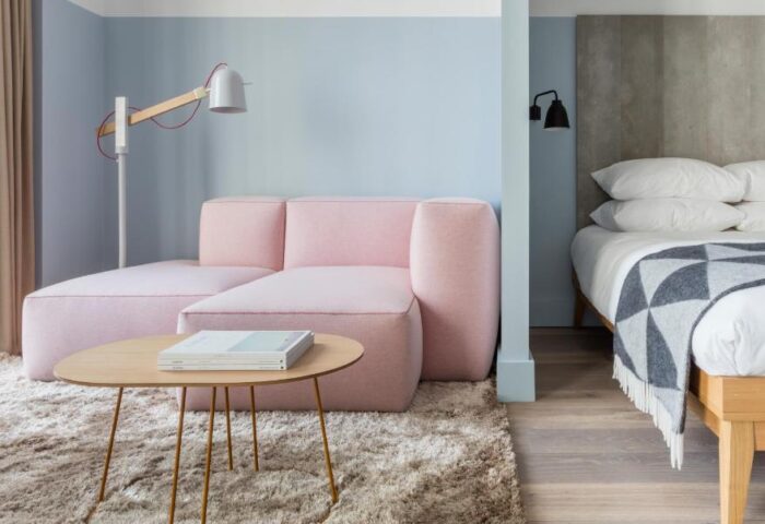 Leman Locke gay-friendly hotel room. Pink sofa, shag rug, & table in the living area. Bed with grey headboard & patterned blanket in the sleeping area.