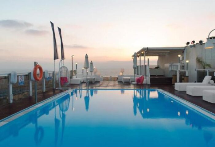 Leonardo Art Tel Aviv By the Beach: Rooftop pool at sunset. Gay-friendly hotel with lounge chairs, umbrellas, and ocean view. Perfect for gay travel.