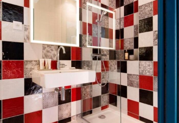 Les Tournelles gay-friendly hotel bathroom. Modern square tile design in red, white, and black. Sink, mirror, and shower.