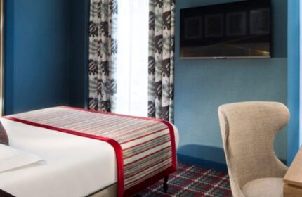 Les Tournelles gay-friendly hotel room. Modern design with blue walls, patterned curtains, and a flat-screen TV. Comfortable chair and stylish bed.