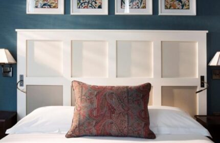 Les Tournelles gay-friendly hotel bedroom. White headboard, paisley pillow, & wall art. Gay travel lodging with style and comfort.