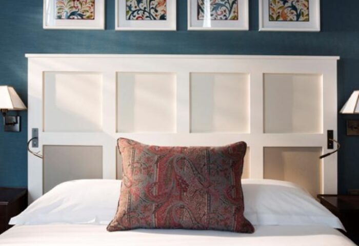 Les Tournelles gay-friendly hotel bedroom. White headboard, paisley pillow, & wall art. Gay travel lodging with style and comfort.