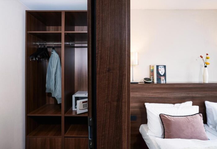 LiV'iN Residence Frankfurt Seilerstraße: Gay-friendly hotel room detail. Closet with safe, bed with pillows, and bedside table with lamp and flowers.