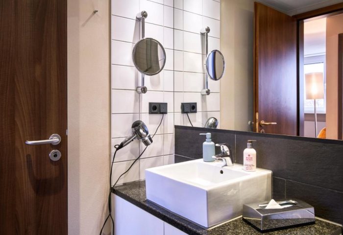 LiV'iN Residence Frankfurt Seilerstraße bathroom. Modern design with sink, mirrors, and amenities. Gay-friendly hotel for men's travel.