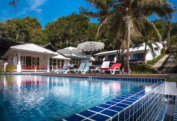 Lima Coco Resort pool view. Gay-friendly hotel with white buildings, palm trees, and blue tiled pool. Ideal for gay travel and relaxation.