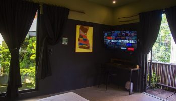Loba Tulum Male Only room interior. Gay-friendly hotel with TV, desk, and balcony. Modern design with dark walls and natural light. Tulum travel.
