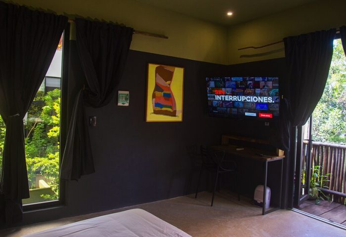 Loba Tulum Male Only room interior. Gay-friendly hotel with TV, desk, and balcony. Modern design with dark walls and natural light. Tulum travel.