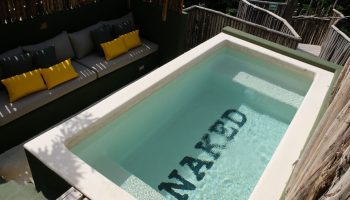 Loba Tulum Male Only gay-friendly hotel pool with NAKED written on the bottom, surrounded by nature. Gay travel in Tulum, Mexico.