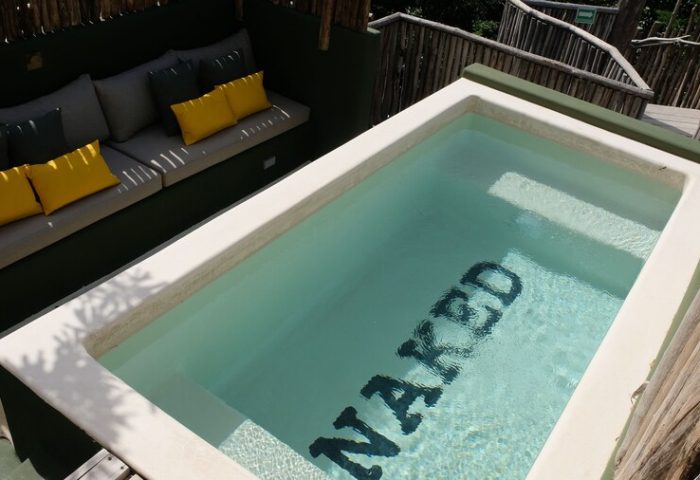 Loba Tulum Male Only gay-friendly hotel pool with NAKED written on the bottom, surrounded by nature. Gay travel in Tulum, Mexico.