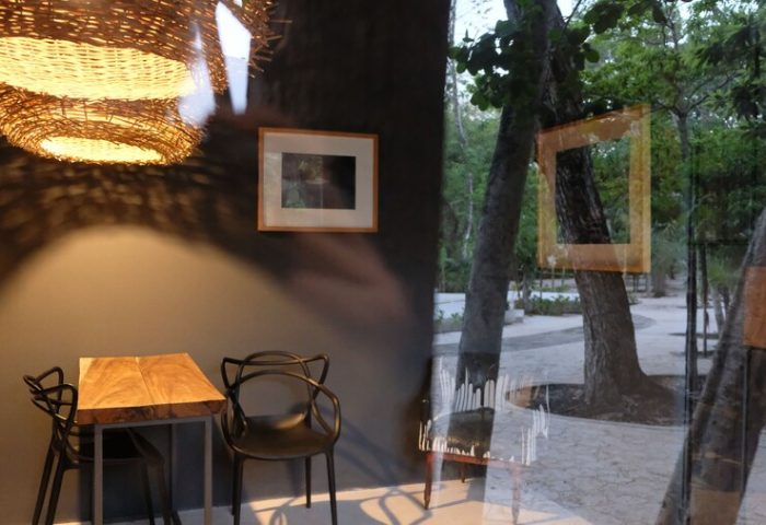 Loba Tulum Male Only gay-friendly hotel interior. Wicker lamp above a table and chairs. View of trees through a window.