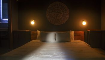 Loba Tulum Male Only gay-friendly hotel room. Bed with white sheets, two pillows, woven wall decor, and warm lighting. Gay travel lodging.