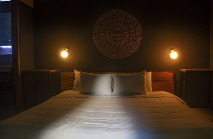 Loba Tulum Male Only gay-friendly hotel room. Bed with white sheets, two pillows, woven wall decor, and warm lighting. Gay travel lodging.