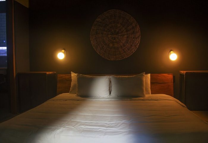Loba Tulum Male Only gay-friendly hotel room. Bed with white sheets, two pillows, woven wall decor, and warm lighting. Gay travel lodging.
