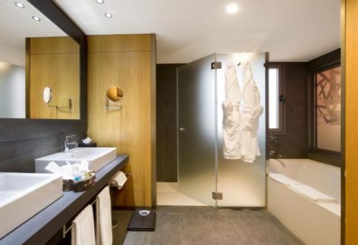 Lopesan Baobab Resort bathroom. Modern design with double sinks, bathtub, and frosted glass shower. Gay-friendly hotel interior.