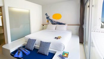 Lub d Phuket Patong gay-friendly hotel room. White bed, boat wall art, blue cushions, fins. Hammock on balcony. Modern design.