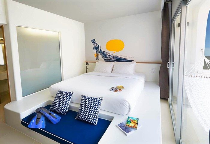 Lub d Phuket Patong gay-friendly hotel room. White bed, boat wall art, blue cushions, fins. Hammock on balcony. Modern design.