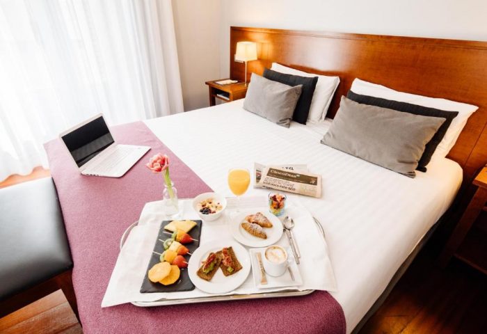 Hotel Infantas by MIJ: Gay-friendly luxury hotel room service. Breakfast tray with laptop, fruit, coffee, and newspaper on the bed. Pet-friendly.