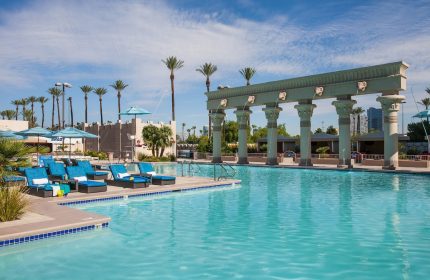 Luxor Hotel pool, a gay-friendly hotel. Turquoise water, palm trees, and Egyptian-themed architecture. Ideal for gay travel in Las Vegas.