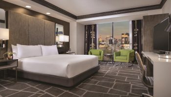 Luxor Hotel room, a gay-friendly hotel. Bedroom view with a king bed, desk, chairs, and the Las Vegas strip visible through the window.