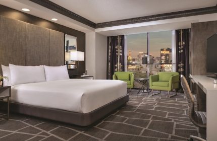 Luxor Hotel room, a gay-friendly hotel. Bedroom view with a king bed, desk, chairs, and the Las Vegas strip visible through the window.