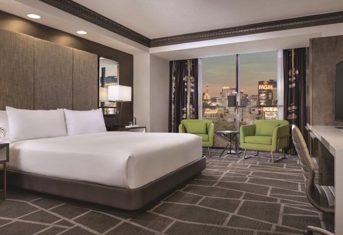 Luxor Hotel room, a gay-friendly hotel. Bedroom view with a king bed, desk, chairs, and the Las Vegas strip visible through the window.