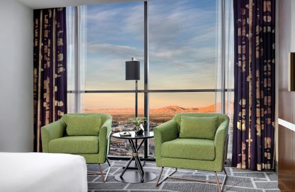 Luxor Hotel room with a view. Two green chairs face a large window overlooking the Las Vegas strip. Gay-friendly hotel for travel advice.