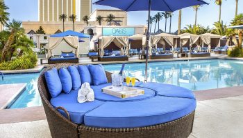 Luxor Hotel pool area, a gay-friendly hotel. Round daybed with blue cushions, poolside cabanas, and a refreshing swimming pool. Oasis sign visible.