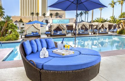 Luxor Hotel pool area, a gay-friendly hotel. Round daybed with blue cushions, poolside cabanas, and a refreshing swimming pool. Oasis sign visible.