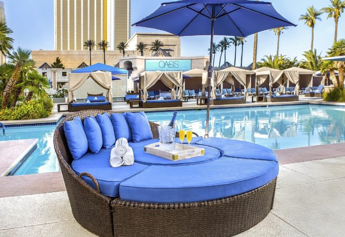 Luxor Hotel pool area, a gay-friendly hotel. Round daybed with blue cushions, poolside cabanas, and a refreshing swimming pool. Oasis sign visible.